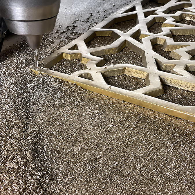 CNC machining of an openwork brass panel with an interlaced Moroccan geometric pattern, metal shavings gathered around the cut