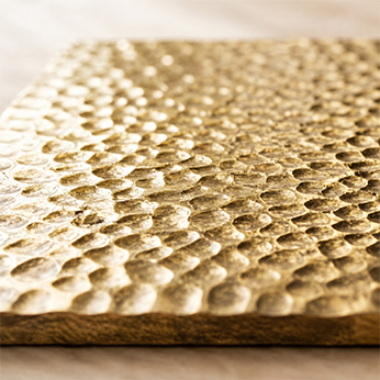 Macro detail of a hammered gold-finish surface with a dimpled texture on the edge of a wood-cored panel