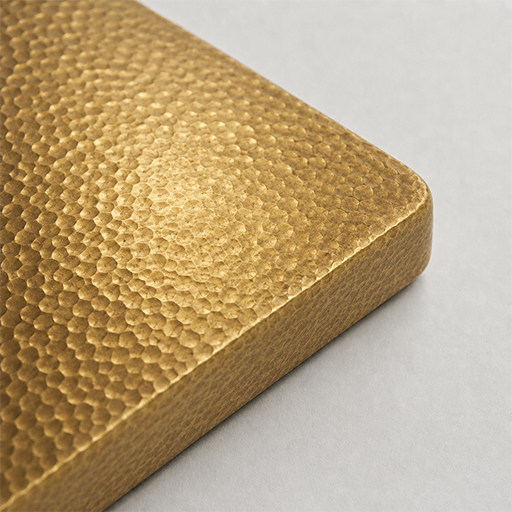 Swatch of a hammered gold-tone finish with a dimpled peened texture in a warm golden hue, shown as a rounded-edge sample block