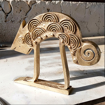 The same spiral-motif animal figure in a matte gold tone, set on a rough stone ledge in the workshop